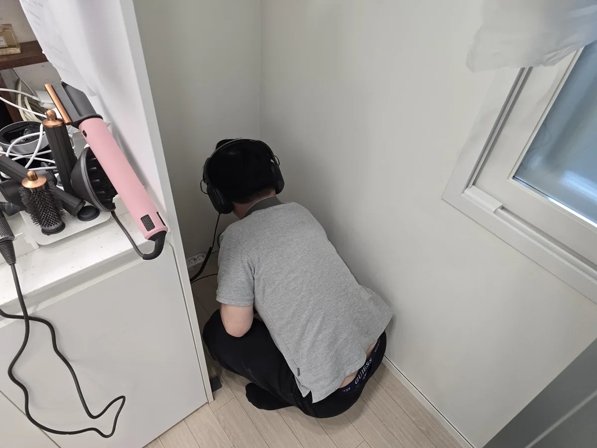 윗집누수탐지 안내 사진, 헤드폰을 쓰고 벽 쪽에서 누수음을 확인하는 기술자